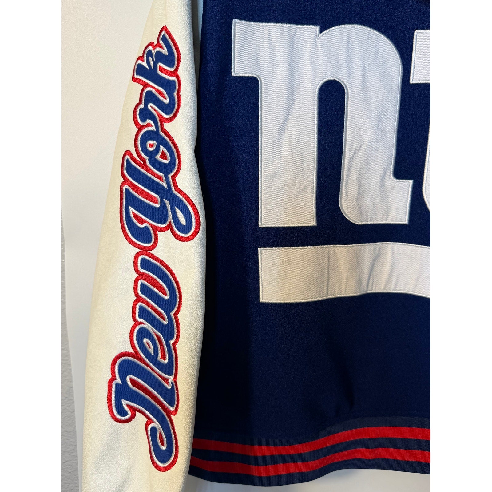 New York Giants women's varsity hooded jacket in blue and white by The Wild Collective, featuring NFL team logo and varsity style.
