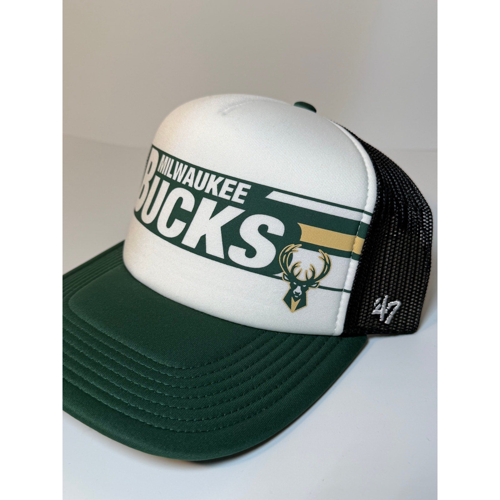 47 Brand Milwaukee Bucks green and white trucker snapback hat with adjustable strap, featuring team logo on front.