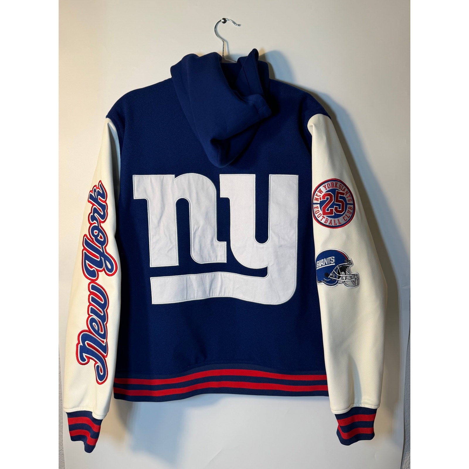 New York Giants women's varsity hooded jacket by The Wild Collective in blue and white, featuring NFL team logo and varsity style.
