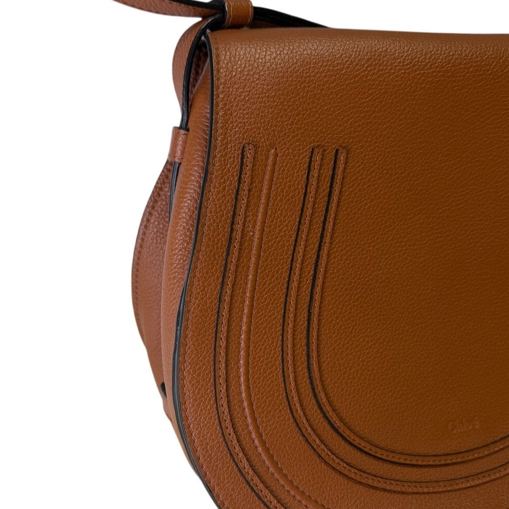 Chloé Marcie medium saddle crossbody handbag in grained calfskin leather with gold hardware, brown color, and adjustable strap.