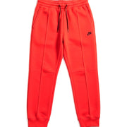 Women's orange Nike Sportswear Tech Fleece joggers with elastic waistband and tapered fit, displayed on a plain background.