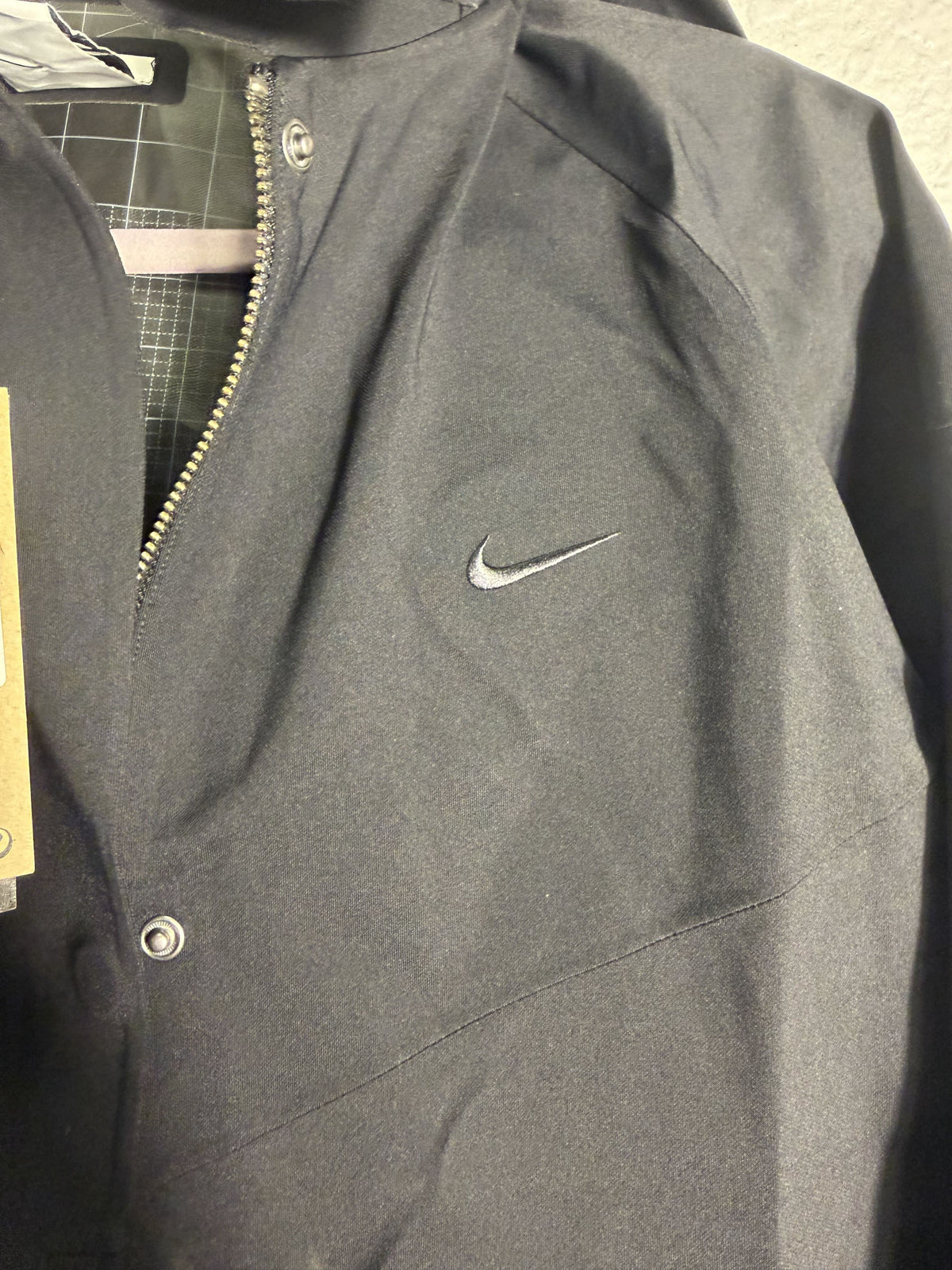 Nike Storm-FIT ADV long trench coat for women in black, showing the sleek, waterproof jacket with a hood and button closures.