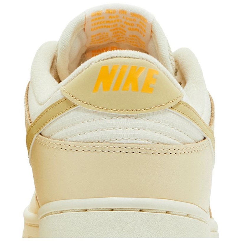 Nike Dunk Low women's sneakers in gold and white, featuring a low-top design and Nike branding.