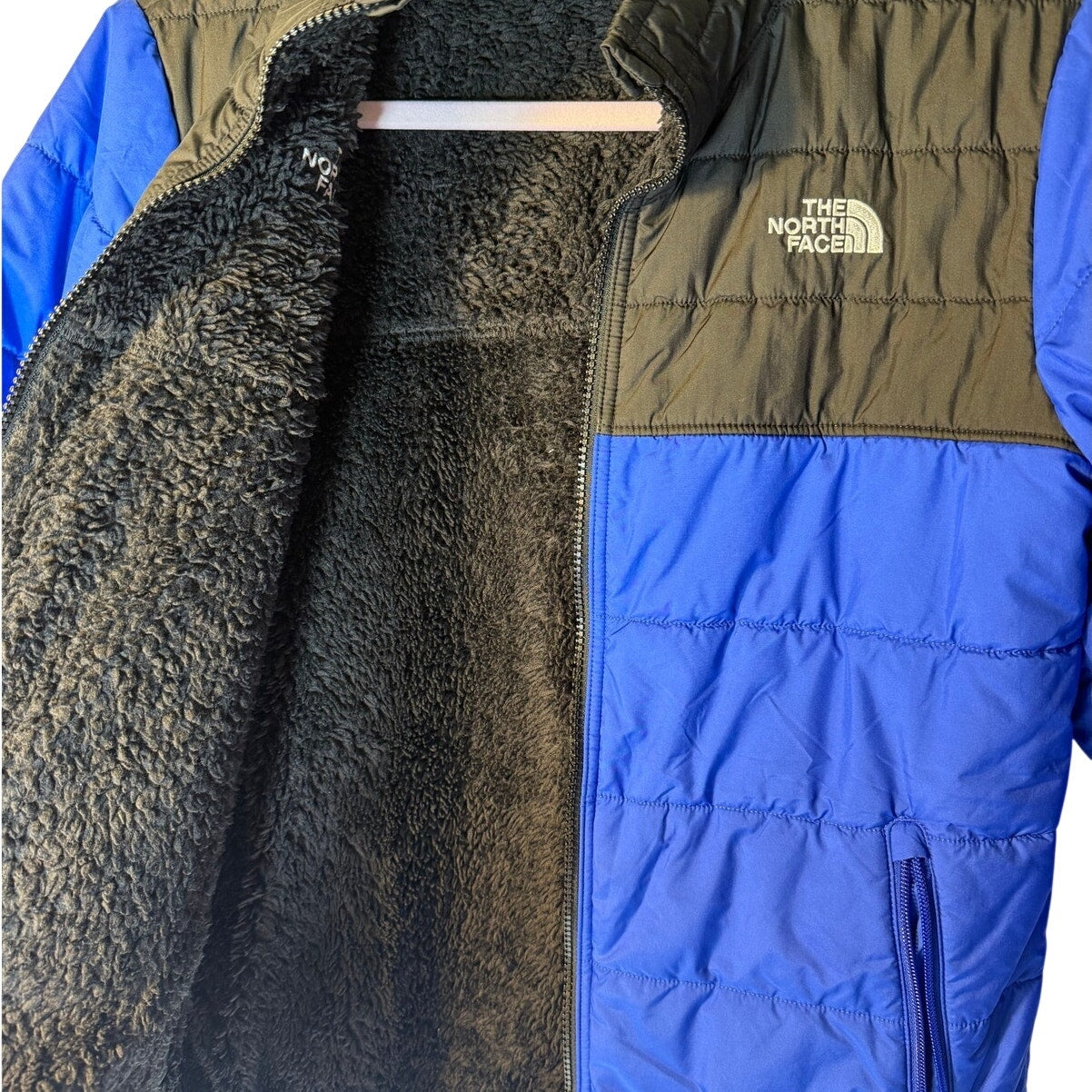 The North Face boys' reversible Mount Chimborazo puffer jacket in size large, blue and black with fleece lining, displayed on a hanger.