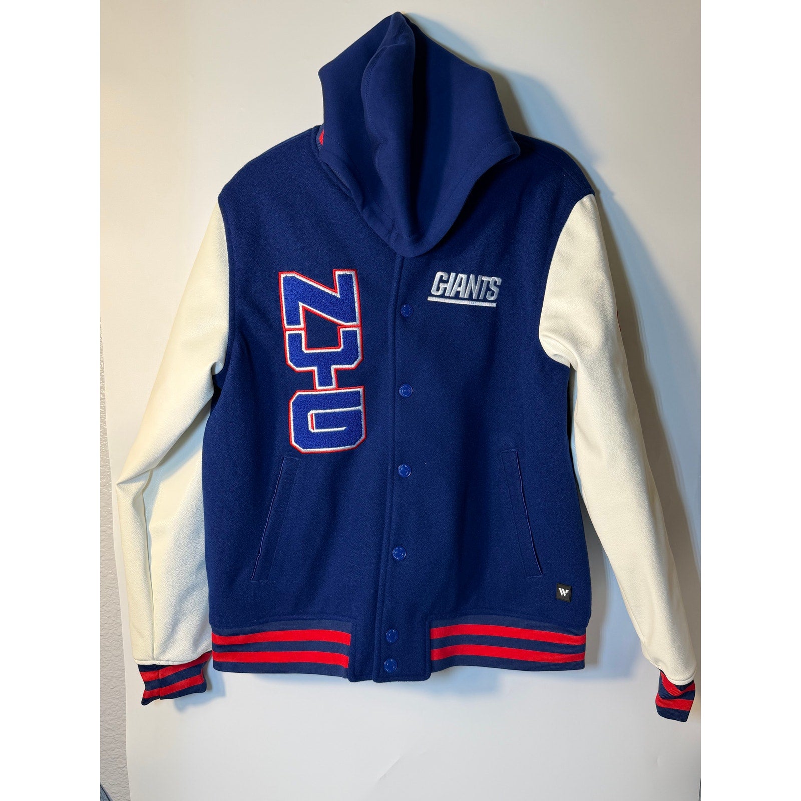 New York Giants women's varsity hooded jacket in blue and white with NFL Wild Collective branding, featuring front pockets and a drawstring hood.