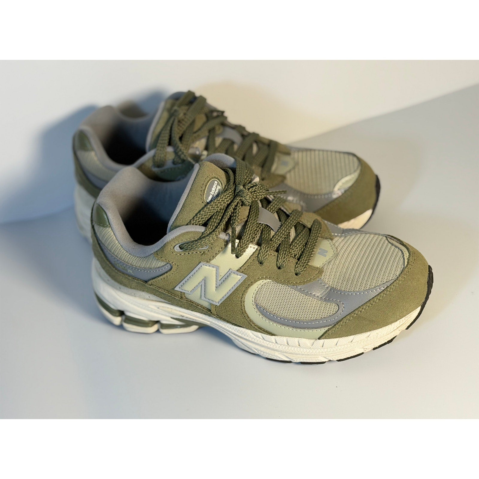 Pre-owned New Balance 2002R athletic sneakers in olive and gray for youth size 5.5, featuring breathable mesh and supportive soles.