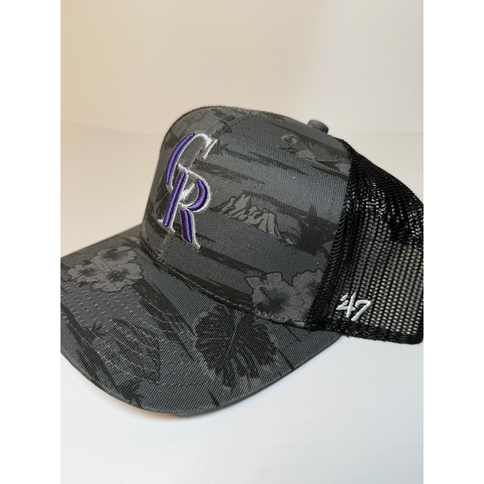 Gray and black 47 Brand Colorado Rockies trucker hat with floral design, adjustable snapback, and mesh back for ventilation.