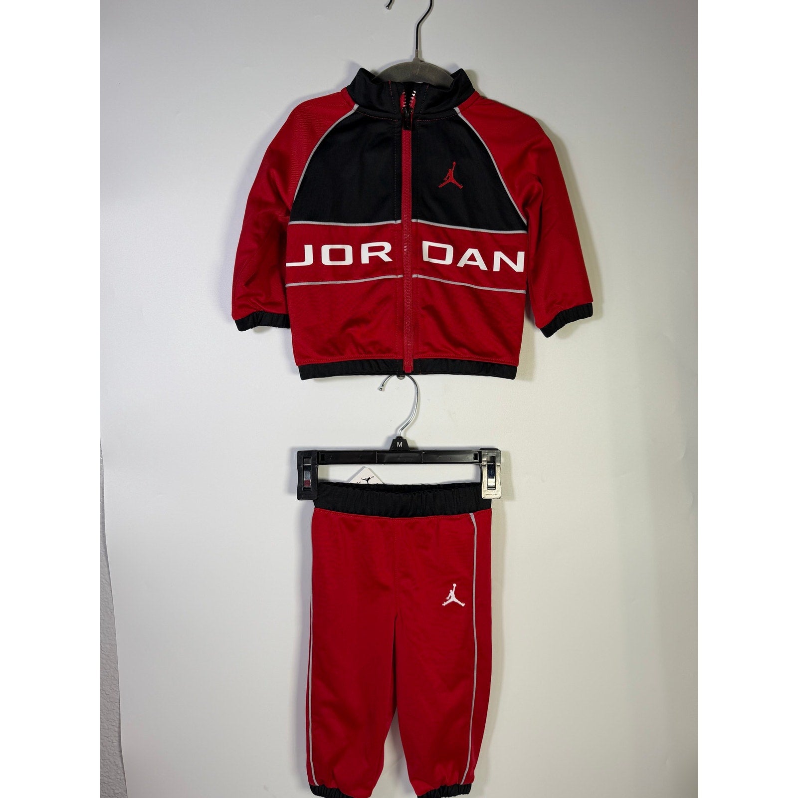 Jordan baby boys 2-piece tracksuit jacket and pants set in red and black for 12 months, displayed on a hanger.