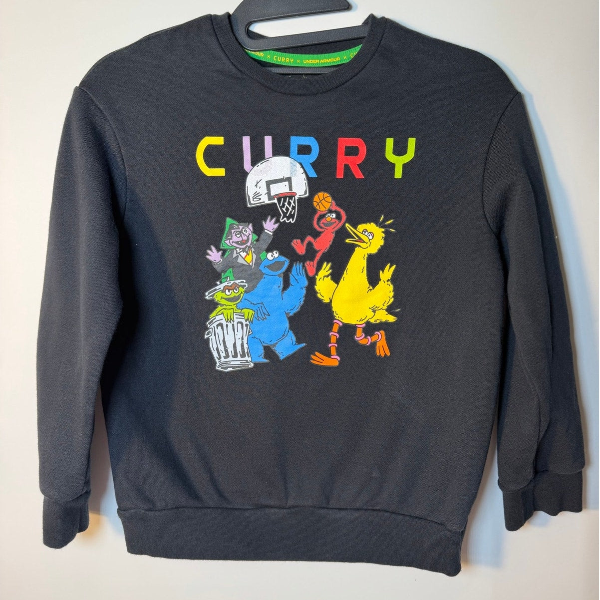 Youth Medium Under Armour Curry Sesame Street black crewneck sweatshirt with colorful Sesame Street characters on the front.