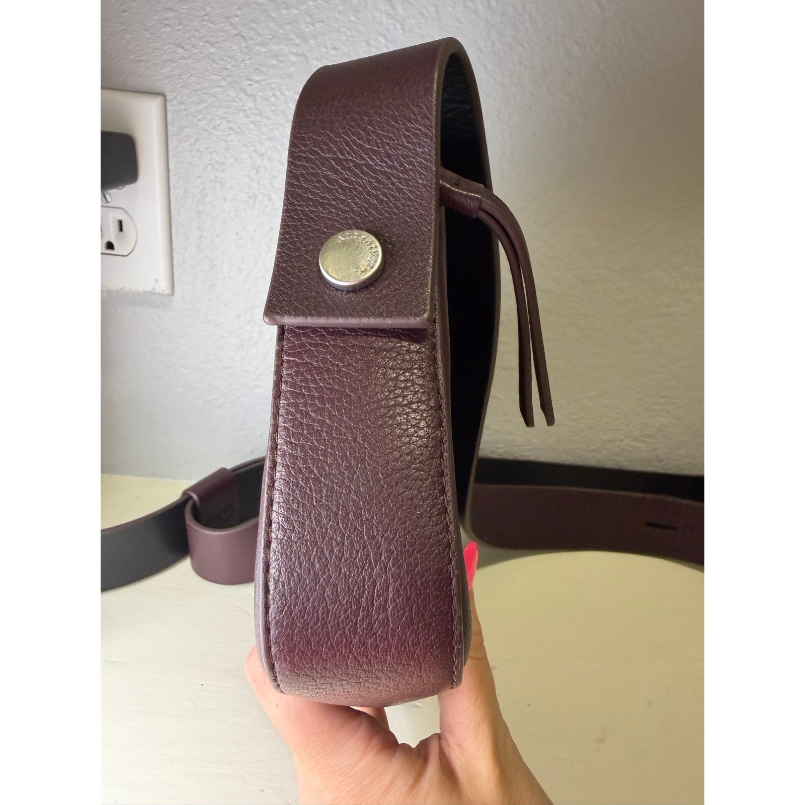 AllSaints women's burgundy pebbled leather camera crossbody handbag with adjustable strap, showcasing the stylish bag's textured leather finish.